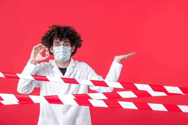 Vista frontal médico masculino sosteniendo matraz con medicamento sobre fondo rojo covid- peligro para la salud uniforme cuarentena color médico