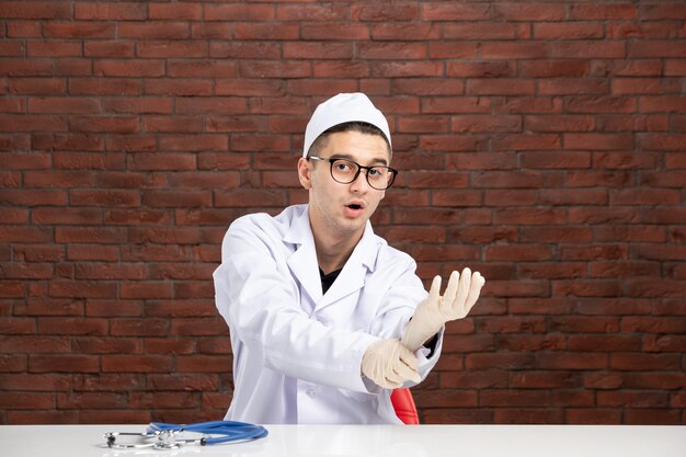 Vista frontal médico masculino en traje médico blanco detrás del escritorio