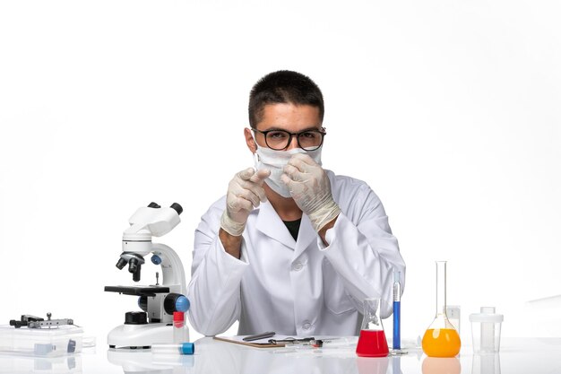 Vista frontal médico masculino en traje médico blanco con máscara debido a covid en el espacio en blanco