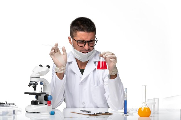 Vista frontal médico masculino en traje médico blanco y con máscara con solución roja en el espacio en blanco