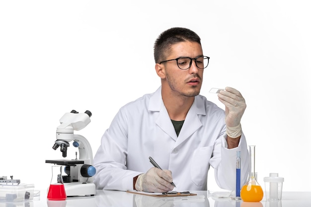 Foto gratuita vista frontal médico masculino en traje médico blanco trabajando con soluciones en espacios en blanco