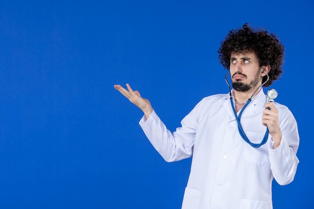 Foto gratuita vista frontal del médico masculino en traje médico con estetoscopio sobre fondo azul salud pandemia covid-virus hospital droga vacuna