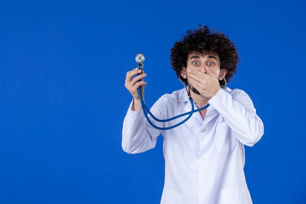 Vista frontal del médico masculino en traje médico con estetoscopio sobre fondo azul vacuna pandemia covid virus salud hospital drogas