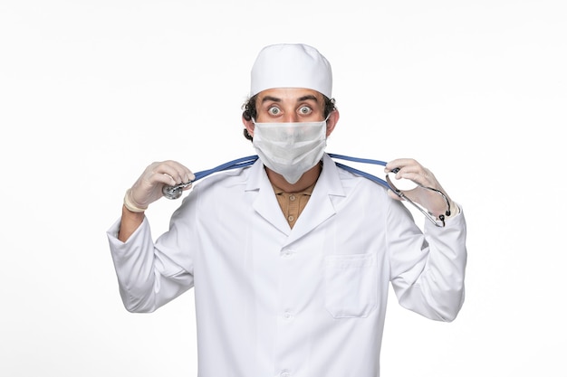 Vista frontal médico masculino en traje médico con máscara como protección contra el covid- en la medicina pandémica de coronavirus de pared blanca