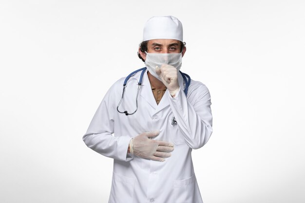 Vista frontal médico masculino en traje médico y con una máscara como protección contra el covid- tos en la pared blanca enfermedad virus covid- pandemia