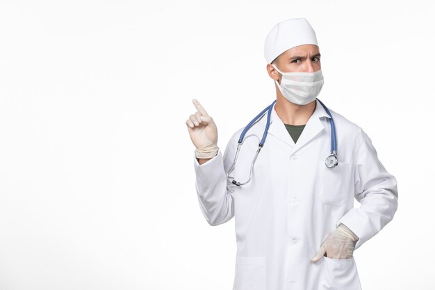 Vista frontal médico masculino en traje médico y con una máscara contra el covid en la pared blanca pandemia de medicina de la enfermedad del virus del covid
