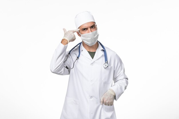 Vista frontal médico masculino en traje médico y con una máscara contra el covid posando en la pared blanca enfermedad covid enfermedad pandémica virus