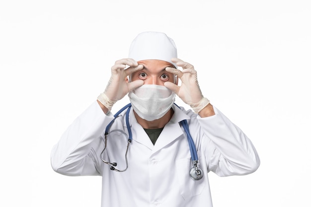Foto gratuita vista frontal médico masculino en traje médico y con máscara debido a covid- en la luz de la pared blanca enfermedad covid- enfermedad pandémica