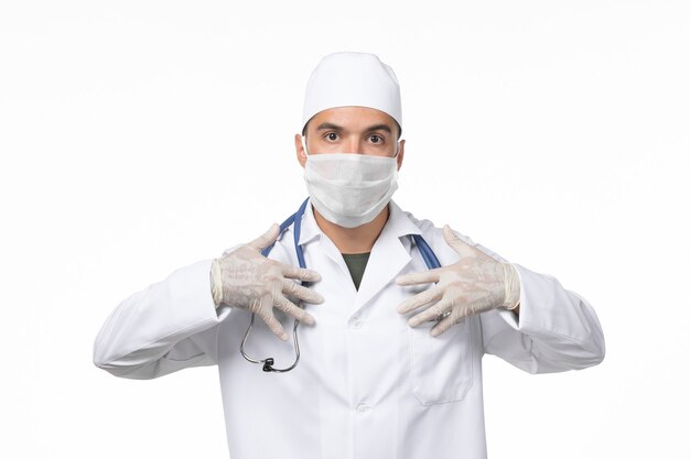 Vista frontal médico masculino en traje médico y con máscara debido a covid- en la pared blanca enfermedad virus covid- enfermedad