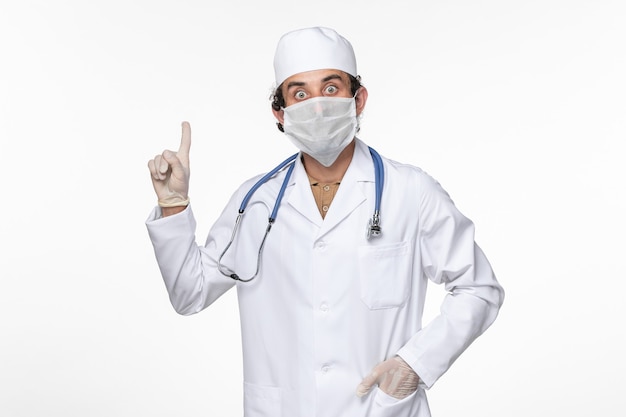 Vista frontal médico masculino en traje médico con máscara estéril como protección contra el covid en la pared blanca virus coronavirus enfermedad pandémica enfermedad