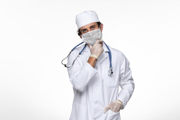 Vista frontal médico masculino en traje médico con máscara estéril como protección contra el covid- pensando en la pandemia del covid