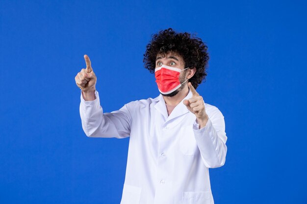 Vista frontal médico masculino en traje médico con máscara roja sobre fondo azul virus del hospital covid-medicina vacuna contra la pandemia