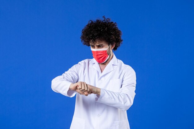 Vista frontal médico masculino en traje médico con máscara roja sobre fondo azul virus del hospital covid-medicina de la vacuna de la salud