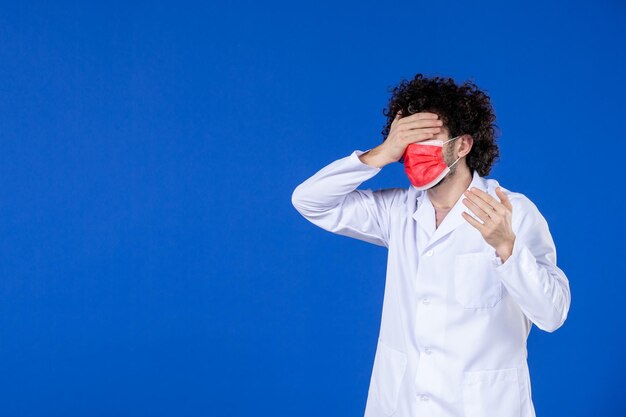 Foto gratuita vista frontal del médico masculino en traje médico y máscara sobre fondo azul vacuna hospital covid salud pandemia coronavirus medicina medicamento