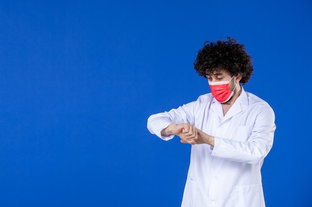 Vista frontal del médico masculino en traje médico y máscara sobre fondo azul vacuna hospital covid- virus salud pandemia coronavirus medicamento medicamento Foto Premium 
