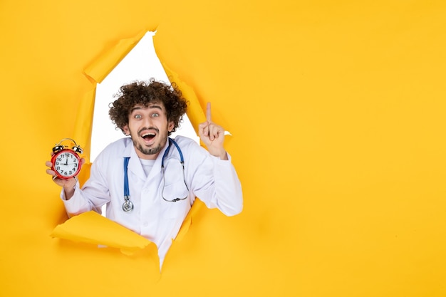 Vista frontal médico masculino en traje médico sosteniendo relojes en medicina amarilla tiempo de salud médico hospital virus