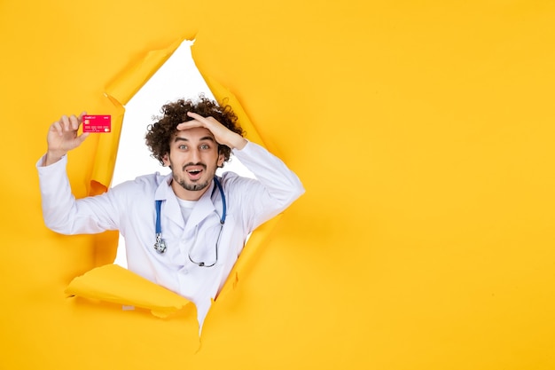 Vista frontal médico masculino en traje médico sosteniendo una tarjeta bancaria roja en la medicina de color amarillo médico del virus de la salud del hospital