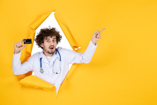 Vista frontal médico masculino en traje médico con tarjeta bancaria en color amarillo rasgado médico medicina hospital enfermedad virus