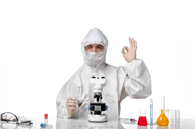 Vista frontal médico masculino en traje de protección y con máscara con microscopio posando en el espacio en blanco