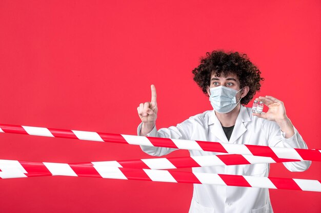 Vista frontal médico masculino en uniforme médico sosteniendo matraces en el fondo rojo franja de color peligro hospital covid- advertencia cuarentena de salud