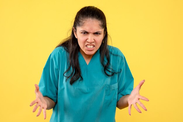 Vista frontal médico mujer nerviosa en uniforme de pie sobre fondo amarillo