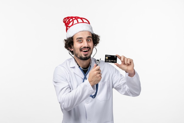 Vista frontal del médico de sexo masculino con estetoscopio y tarjeta bancaria en la pared blanca