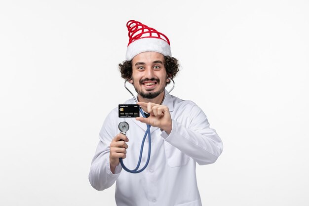 Vista frontal del médico de sexo masculino con estetoscopio y tarjeta bancaria en la pared blanca