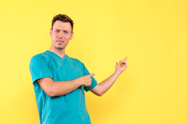 Vista frontal del médico de sexo masculino con expresión confusa en la pared amarilla