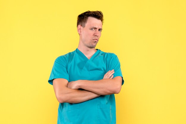 Vista frontal del médico de sexo masculino con expresión de disgusto en la pared amarilla