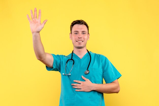 Vista frontal del médico de sexo masculino con expresión emocionada en la pared amarilla