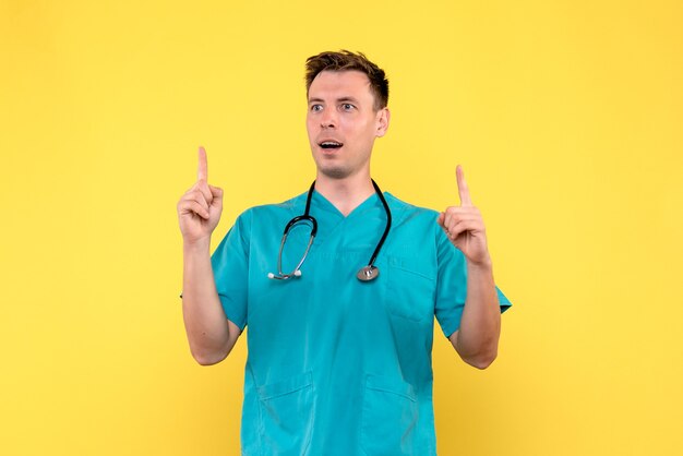 Vista frontal del médico de sexo masculino con expresión emocionada en la pared amarilla
