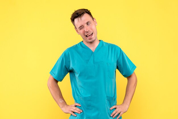 Vista frontal del médico de sexo masculino con expresión de guiño en la pared amarilla