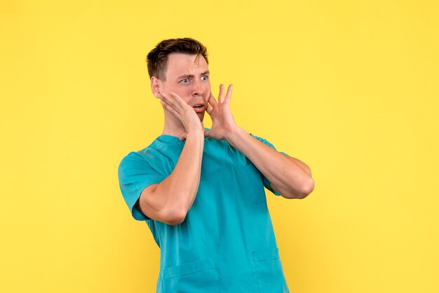 Vista frontal del médico de sexo masculino con expresión de miedo en la pared amarilla