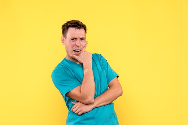 Vista frontal del médico de sexo masculino con expresión de pensamiento en la pared amarilla