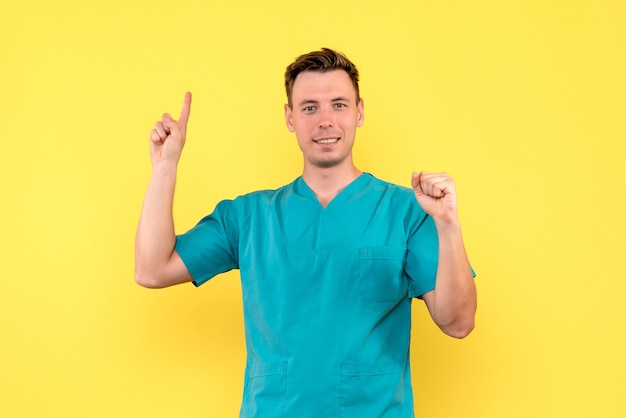 Vista frontal del médico de sexo masculino con expresión sonriente en la pared amarilla