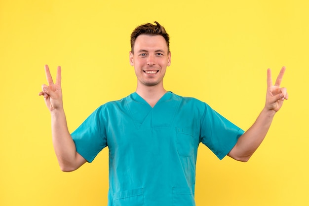 Vista frontal del médico de sexo masculino con expresión sonriente en la pared amarilla