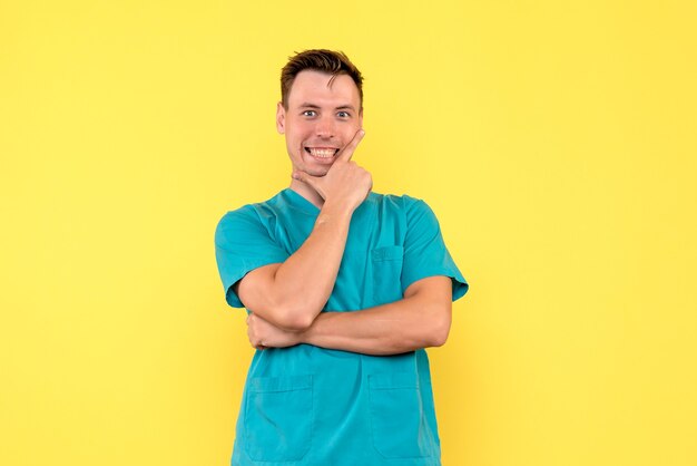 Vista frontal del médico de sexo masculino con expresión sonriente en la pared amarilla