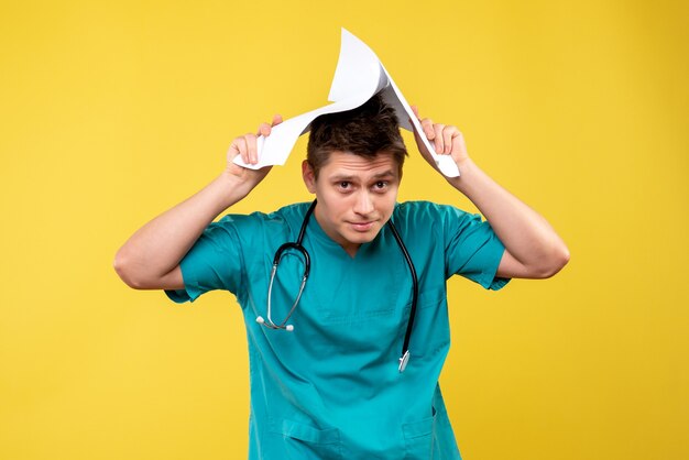 Vista frontal del médico de sexo masculino en traje médico con análisis en la pared amarilla
