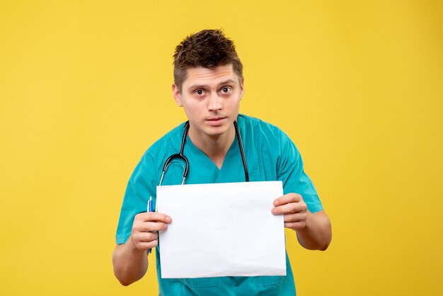 Vista frontal del médico de sexo masculino en traje médico con análisis en la pared amarilla