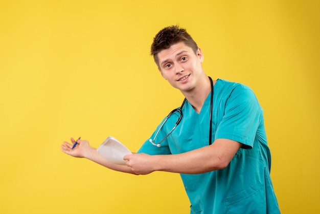 Vista frontal del médico de sexo masculino en traje médico con análisis en la pared amarilla