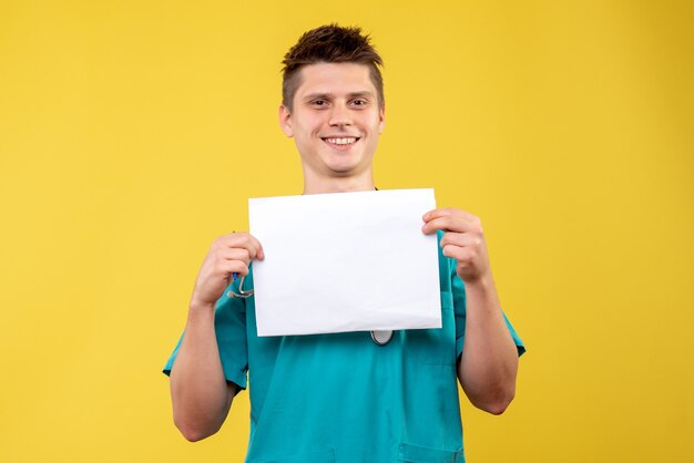 Vista frontal del médico de sexo masculino en traje médico con análisis en la pared amarilla