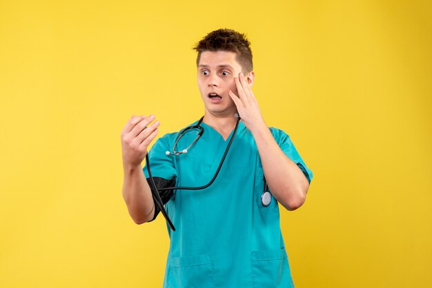 Vista frontal del médico de sexo masculino en traje médico comprobando su presión sobre la pared amarilla