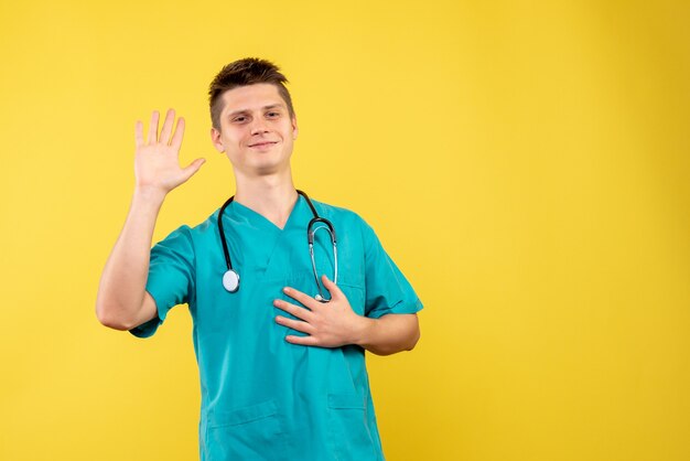 Vista frontal del médico de sexo masculino en traje médico con estetoscopio en la pared amarilla