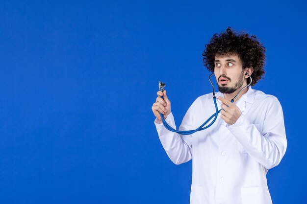 Vista frontal del médico de sexo masculino en traje médico con estetoscopio sobre superficie azul