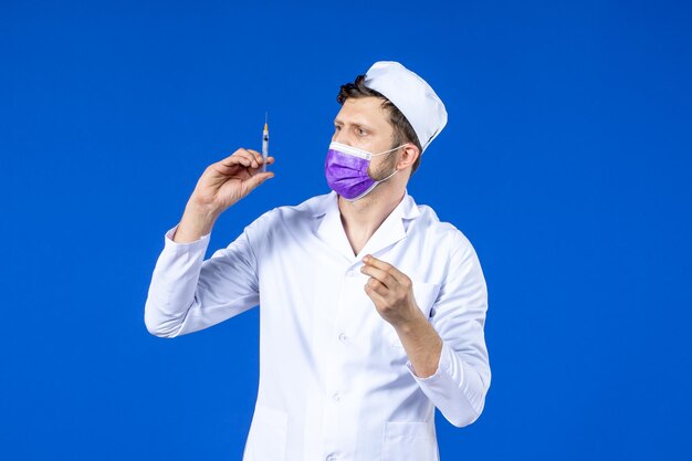 Vista frontal del médico de sexo masculino en traje médico y inyección de llenado de máscara con vacuna en azul