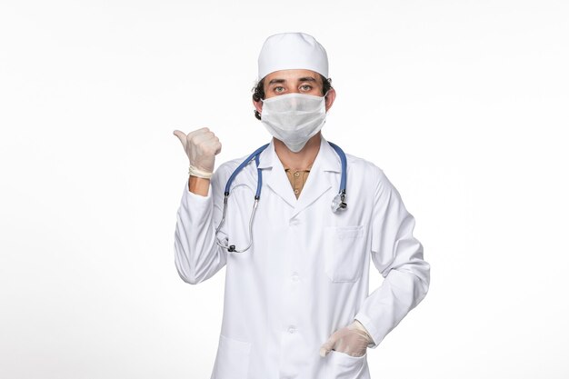 Vista frontal médico de sexo masculino en traje médico con máscara como protección contra covid- en la pared blanca clara virus salpicadura pandemia de coronavirus