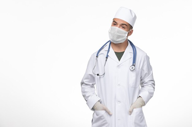 Vista frontal médico de sexo masculino con traje médico y máscara contra el coronavirus en la pared blanca clara, enfermedad del virus covid, enfermedad, aislamiento, pandemia