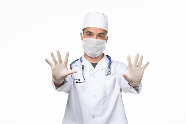 Vista frontal médico de sexo masculino con traje médico y máscara contra el coronavirus en la pared blanca, enfermedad del virus covid, enfermedad, aislamiento, pandemia