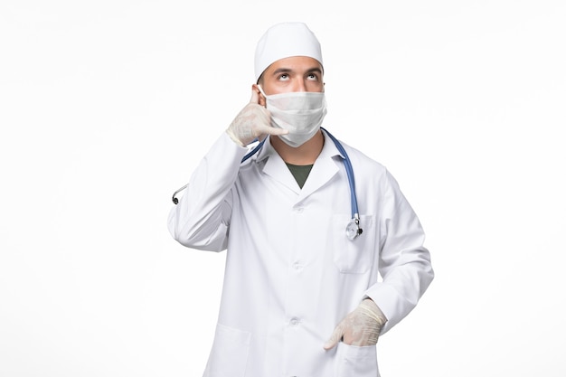 Vista frontal médico de sexo masculino en traje médico y con una máscara contra el covid en el escritorio ligero virus de la pandemia de la medicina de la enfermedad del covid