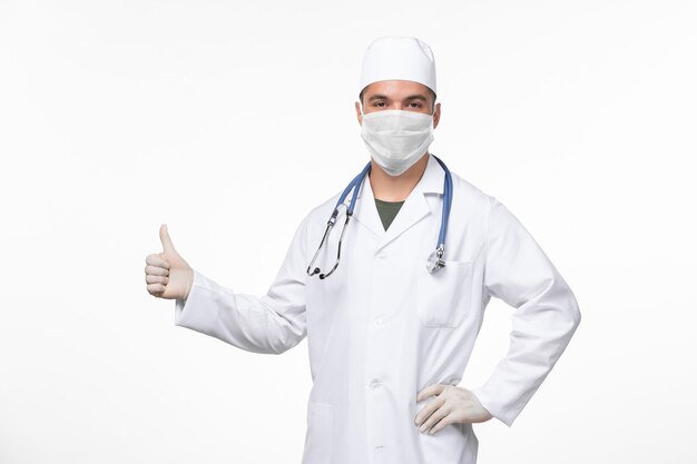Vista frontal médico de sexo masculino en traje médico y con una máscara contra el covid sonriendo en la pared blanca virus covid enfermedad pandemia